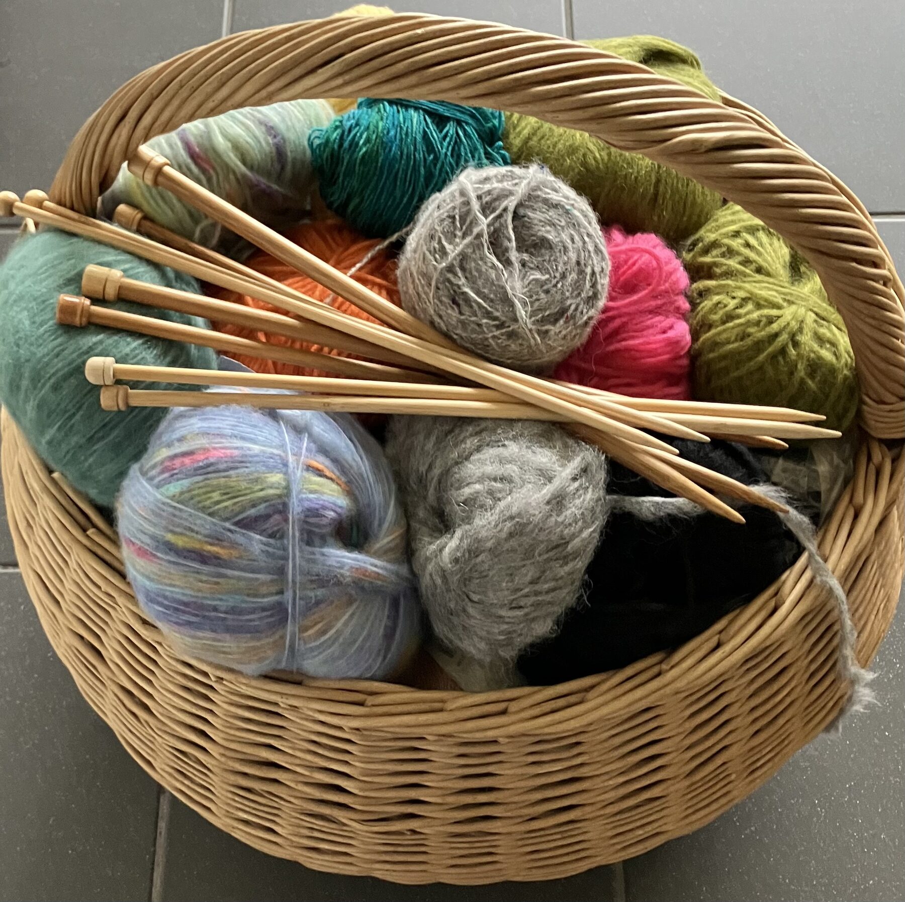 Weidenkorb mit Wollknäueln in vielen Farben und Stricknadeln aus Holz
